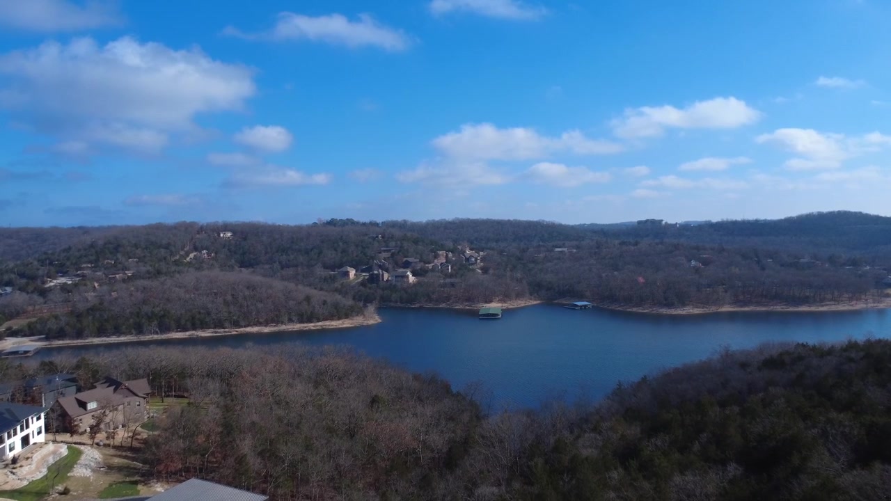 A sweeping aerial view reveals a peaceful lake surrounded by rolling Ozark hills and dense forest.