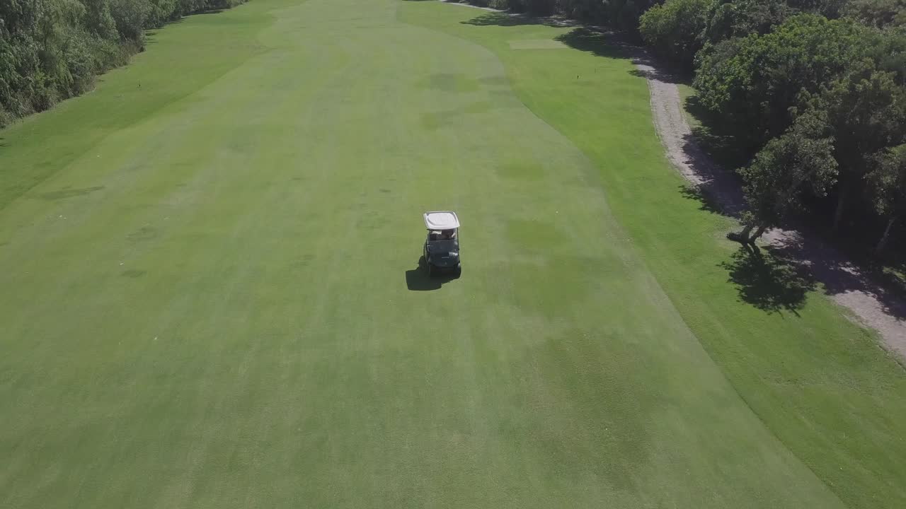 Retreating tracking aerial of golf card driving down green fairway