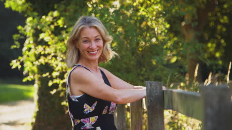 portrait of casually dressed mature woman leaning on fence on walk in countryside