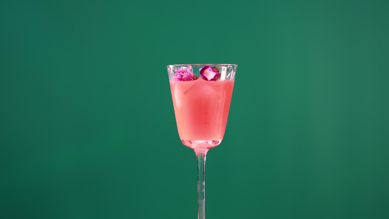 A pink cocktail with ice and garnish in a glass, set against a green screen, showcasing minimal movement