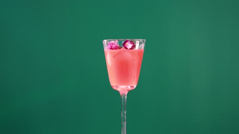 a pink cocktail with ice and garnish in a glass, set against a green screen, showcasing minimal movement