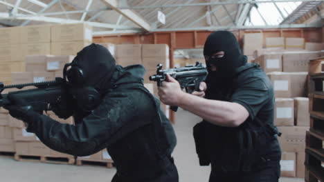 a police swat team searches a warehouse with guns drawn wearing balaclavas an gas masks