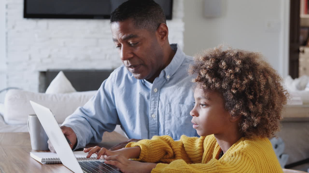 Pre-teen African American girl sitting at a table working on a laptop computer with her home tutor, close up