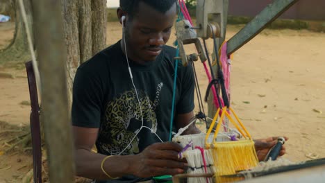 worker from ghana hand knitting kente cloths while listening music