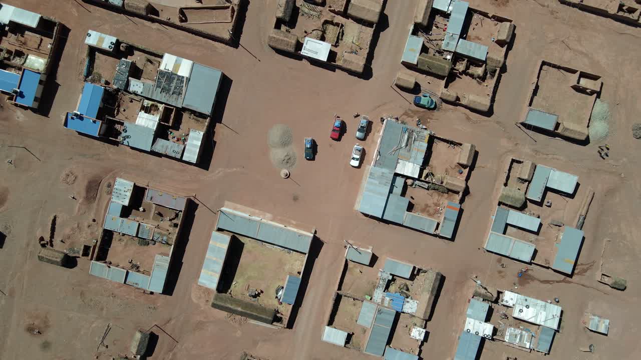 Aerial top down ascend above a remote Bolivian highland village built on reddish terrain in desert climate
