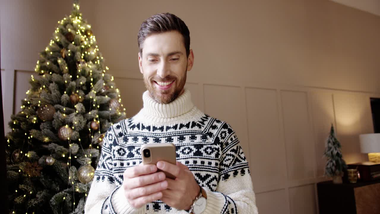 joven alegre y sonriente enviando mensajes de texto por teléfono celular enviando saludos y mejores deseos en la víspera de navidad