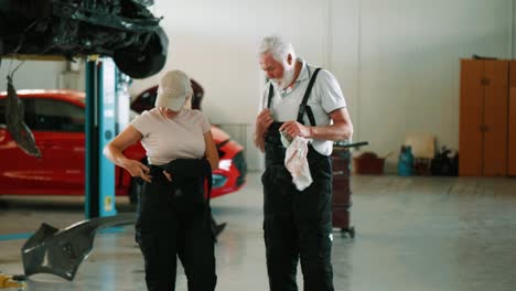 mecánico anciano y mujer se quitan los uniformes después de terminar el trabajo en el servicio de automóviles. colegas mecánicos hablan al final de las horas de trabajo mientras caminan