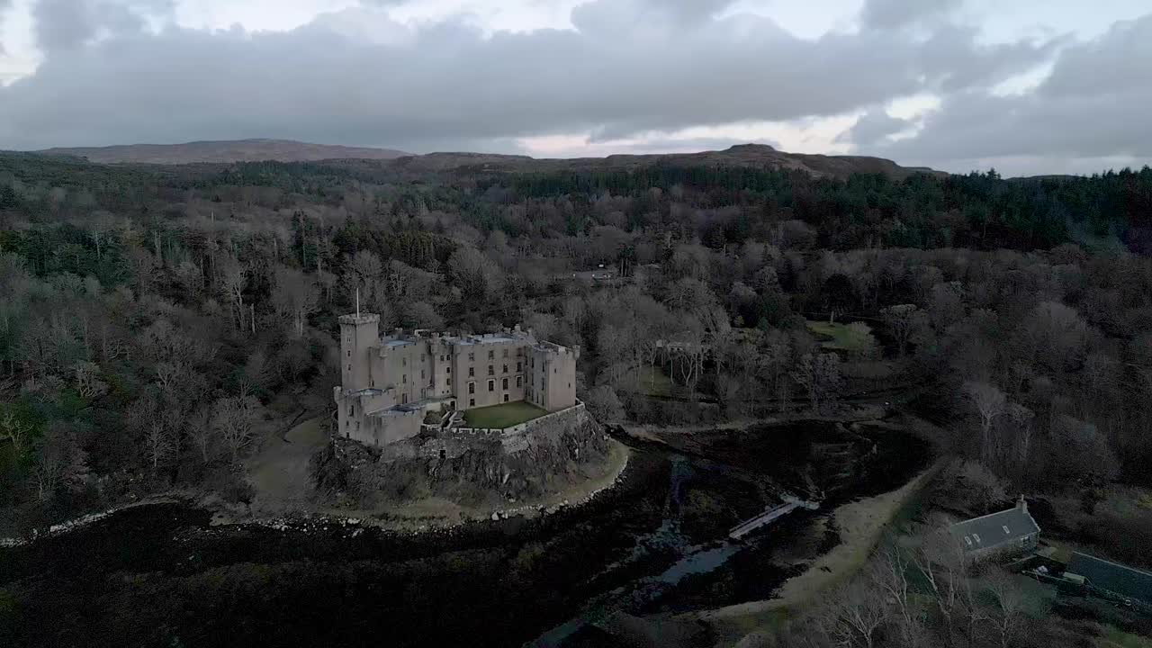 el castillo de dunvegan en la isla de skye rodeado de bosques en clima nublado, vista aérea