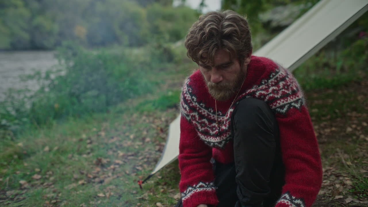 Man Roasting Skewered Meat over Fire at Forest Campsite by River