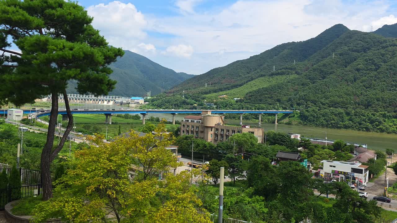 Shot shifts from panoramic view of Sincheongpyeongdae Bridge, Bukhangang River and Hwayasan Mountain in Gapyeong to the cozy yard garden of a local cafe