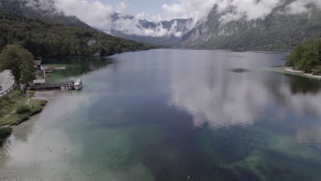 front descriptive panning drone video on lake bohinj passing over the most bridge with people and vehicles circulating, ending with the horizon in the mountains