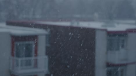 Concéntrese-En-La-Nieve-De-Invierno-A-Cámara-Lenta-Que-Cae-Con-El-Edificio-Exterior-En-Segundo-Plano