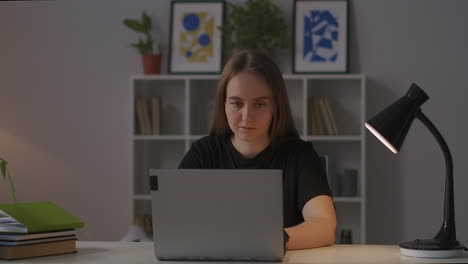 joven encantadora está usando internet por portátil por la noche descansando en casa y navegando por las redes sociales sentada en la mesa en la sala de estar retrato medio