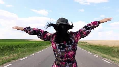 a happy woman feeling the air while walking in an empty countryside highway