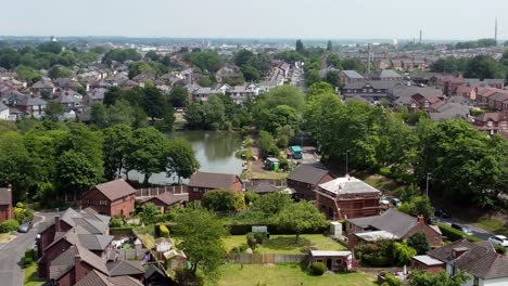 Aerial-view-descending-to-red-brick-British-townhouse-neighbourhood-development-with-lake-as-builders-work-on-rooftop-renovation