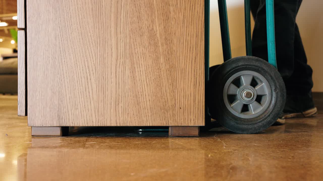 Man uses a hand truck to lift and move a wooden dresser out of frame