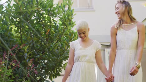 Happy-diverse-female-couple-holding-hands-and-embracing-in-garden