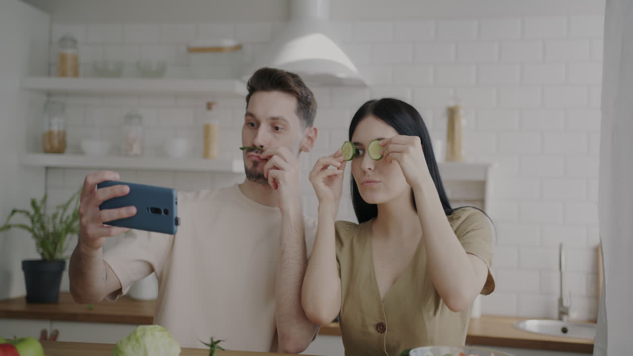 Couple taking a silly selfie in the kitchen with cucumber
