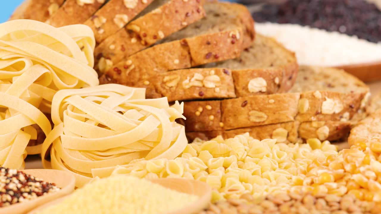 A vibrant display of various grains, pasta, and sliced bread arranged in a well-lit setting