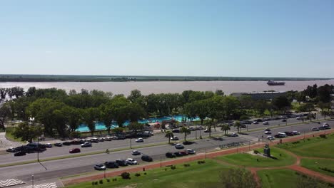 an aerial view captures a coastal avenue with car traffic and the river in the background on a sunny morning, highlighting the vibrant city life.