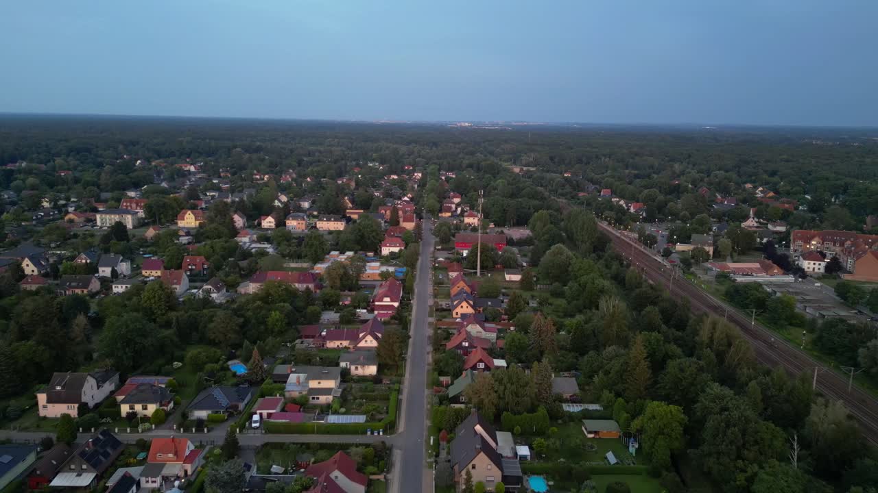 sunset residential area in Brandenburg, Germany, showcasing rooftops, lush greenery, and a network of roads. Unbelievable aerial view flight fly reverse drone