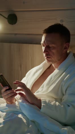 relaxing evening in a cozy room with a man checking his phone in a bathrobe