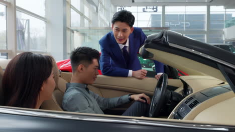 couple with attractive auto dealer in a suit presenting new car model to his client