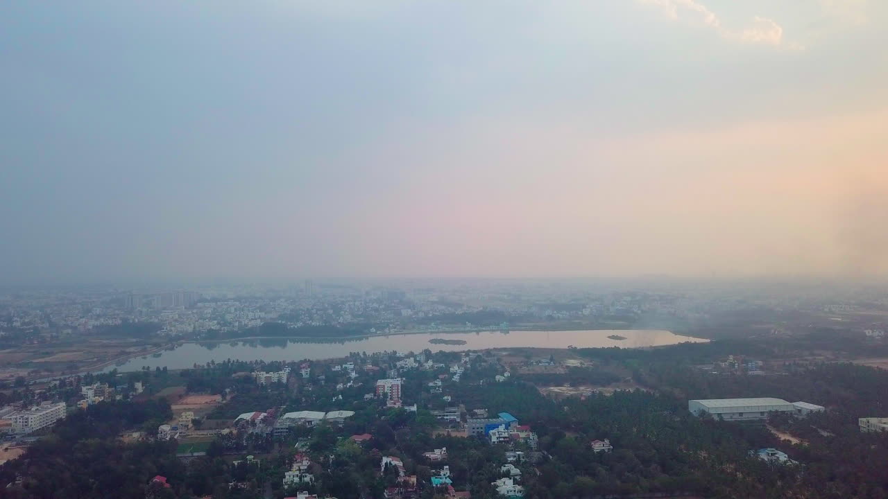 Pull back aerial shot of Bangalore city covered in greenery and Kalkere Lake in Karnataka, India.