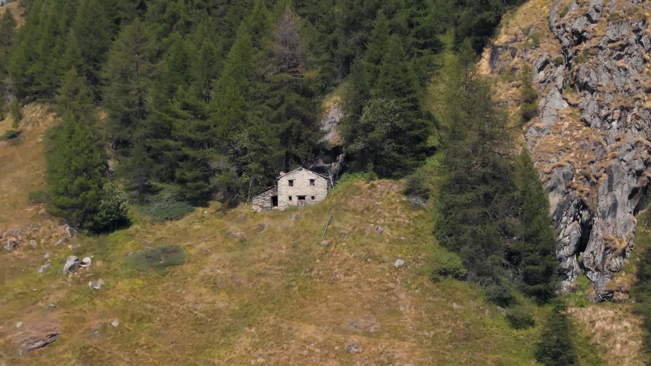 Pulling back aerial drone view of a mountain house in Valtournenche, Aosta Valley, Valle d’Aosta, surrounded by a dense pine forest