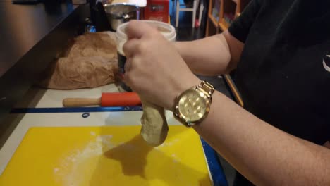 las manos de la trabajadora con reloj dorado amasando masa con harina de trigo para preparar pizza en el horno, el área de trabajo de su negocio de catering, toma de foco, pedidos, galicia, españa