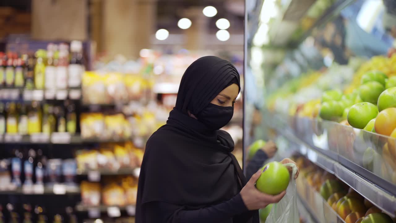 mujeres musulmanas comprando comestibles, tomando frutas de la estantería, vista lateral