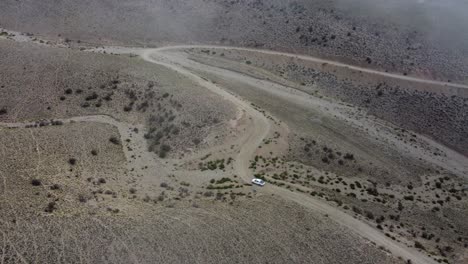 Flight-through-cloud,-lone-truck-drives-on-twisted-arid-dirt-road