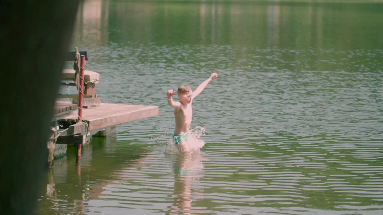 목조 부두에서 호수로 점프하는 백인 아이가 부족하여 느린 팬