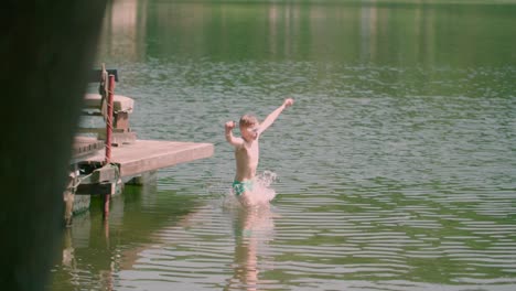 Slow-pan-over-short-of-a-Caucasian-kid-jumping-from-the-wooden-pier-into-the-lake