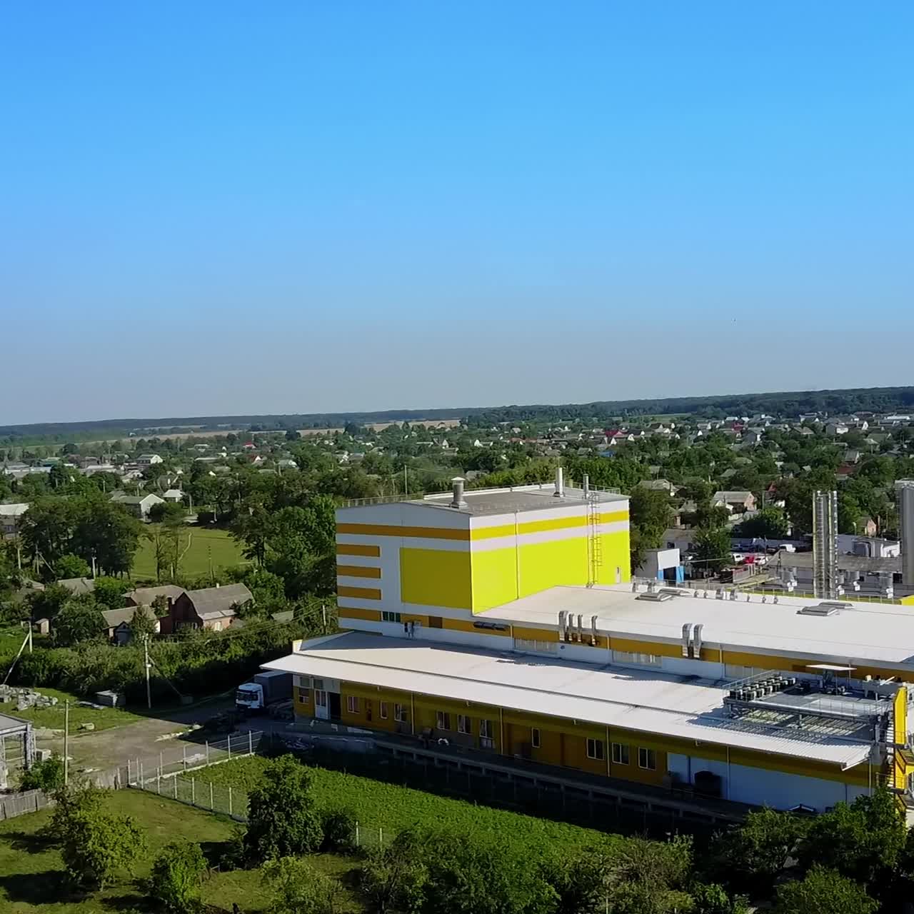 Big white and yellow building of an industrial plant located in the rural area. Aerial perspective. Blue clear sky at backdrop