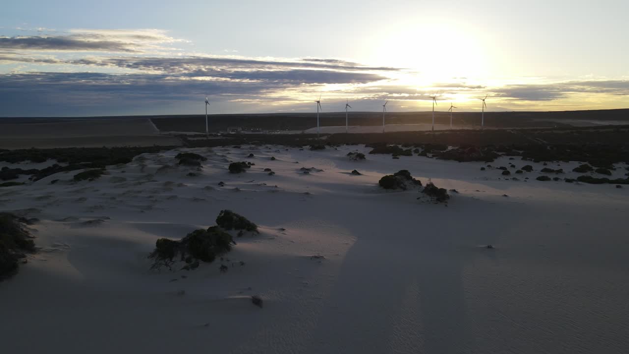 Drone aerial near windmills panning right during a sunrise with sand dunes