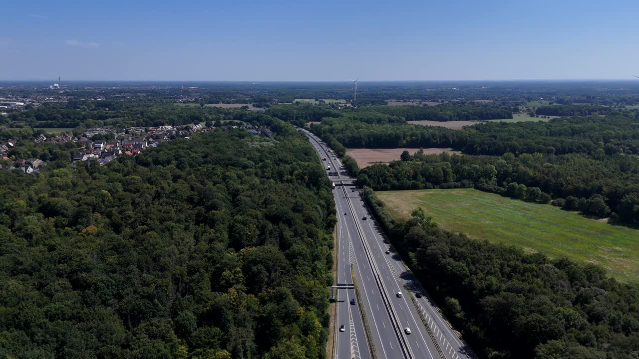 Driving cars and vehicles on multi-lane highway between green trees in America. Drone wide shot. Small neighborhood city and farm fields in summer. Blue sky and sun. Busy intersection in suburb, USA