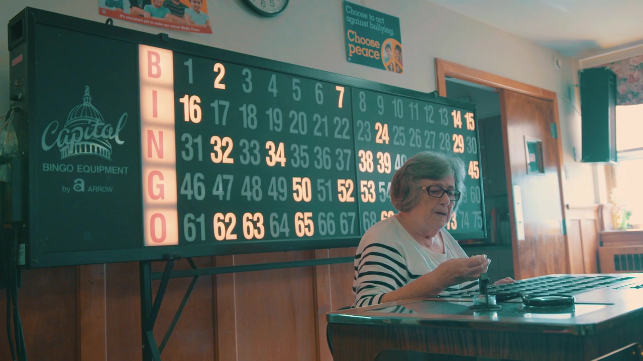 An elderly women, runs a quiet bingo hall during the day, in slow motion.