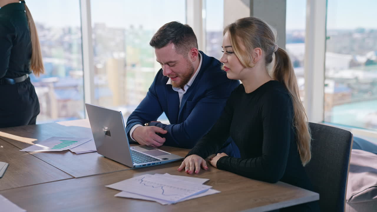 Young businessman and woman in office. Beautiful woman entrepreneur and a handsome man sitting at the table and looking into laptop in business center.