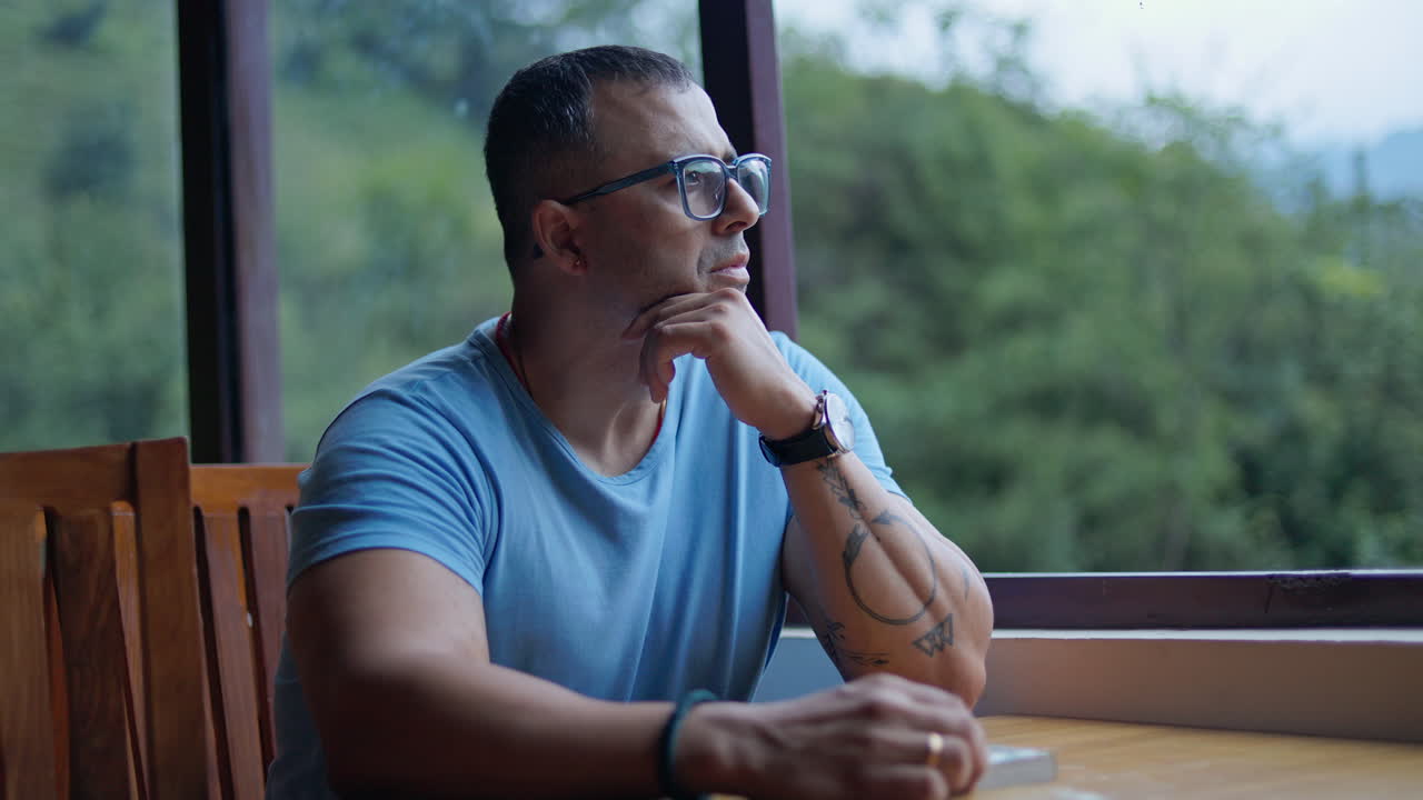 Man spending leisure time in countryside café, sitting quietly and thinking while enjoying outdoor scenery