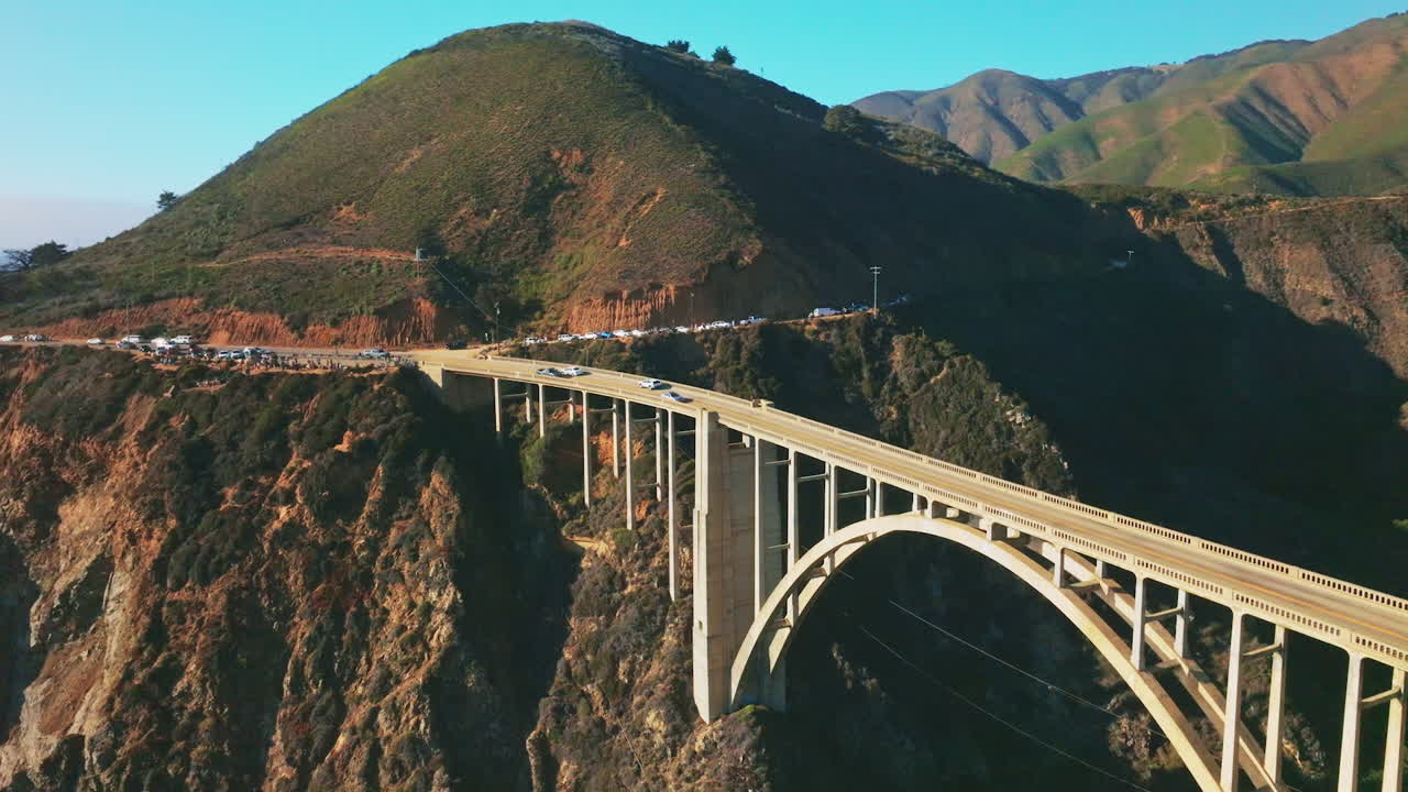 Busy road around the rugged mountain passing into the beautiful arched bridge over the gap in the rocks. Blue skies at backdrop. Top view.
