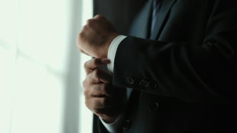 hombre de negocios confiado en el clásico traje azul abotonado o ajustar gemelos cerca de la ventana en la habitación del hotel por la mañana. hombre guapo con un buen traje en el día de la boda.