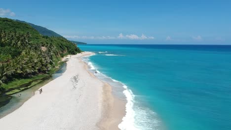 vista aérea ascendente desde drones mientras la gente camina en una playa estrecha con un océano azul brillante en un lado y un río claro y fresco alimentado por manantiales de montaña en el otro