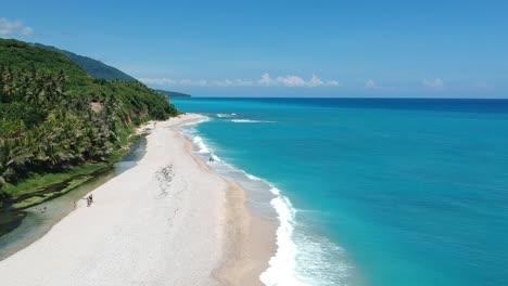 ascending aerial view from drone as people walk on a narrow beach with bright blue ocean on one side and clear cool mountain spring fed river on the other