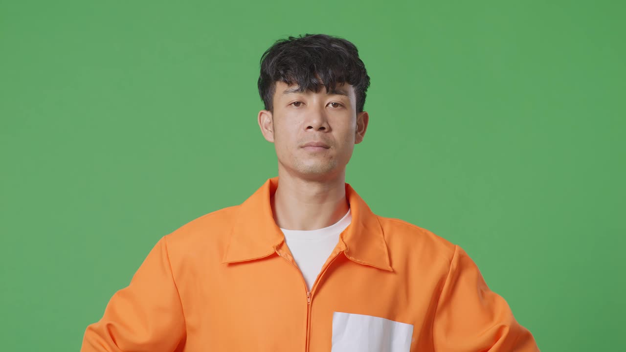 녹색 스크린 배경에서 머리를 들고 카메라를 바라보며 팔을 들고 서 있는 아시아 남성 수감자의 클로즈업