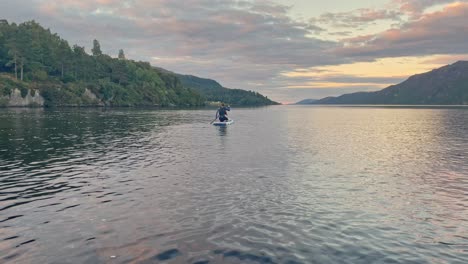 young woman in a wetsuit paddleboarding on a stand up paddleboard into the sunny horizon on loch ness