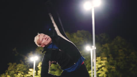 sportive blond man doing stretching exercises before training in the park at night 1