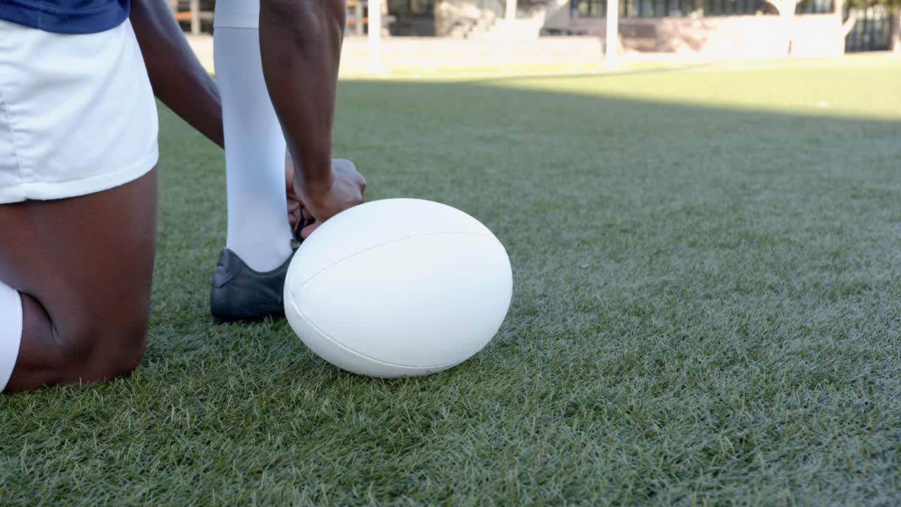 Kneeling on grass, rugby african american male player preparing to kick white rugby ball, copy space