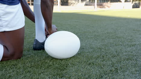 kneeling on grass, rugby african american male player preparing to kick white rugby ball, copy space