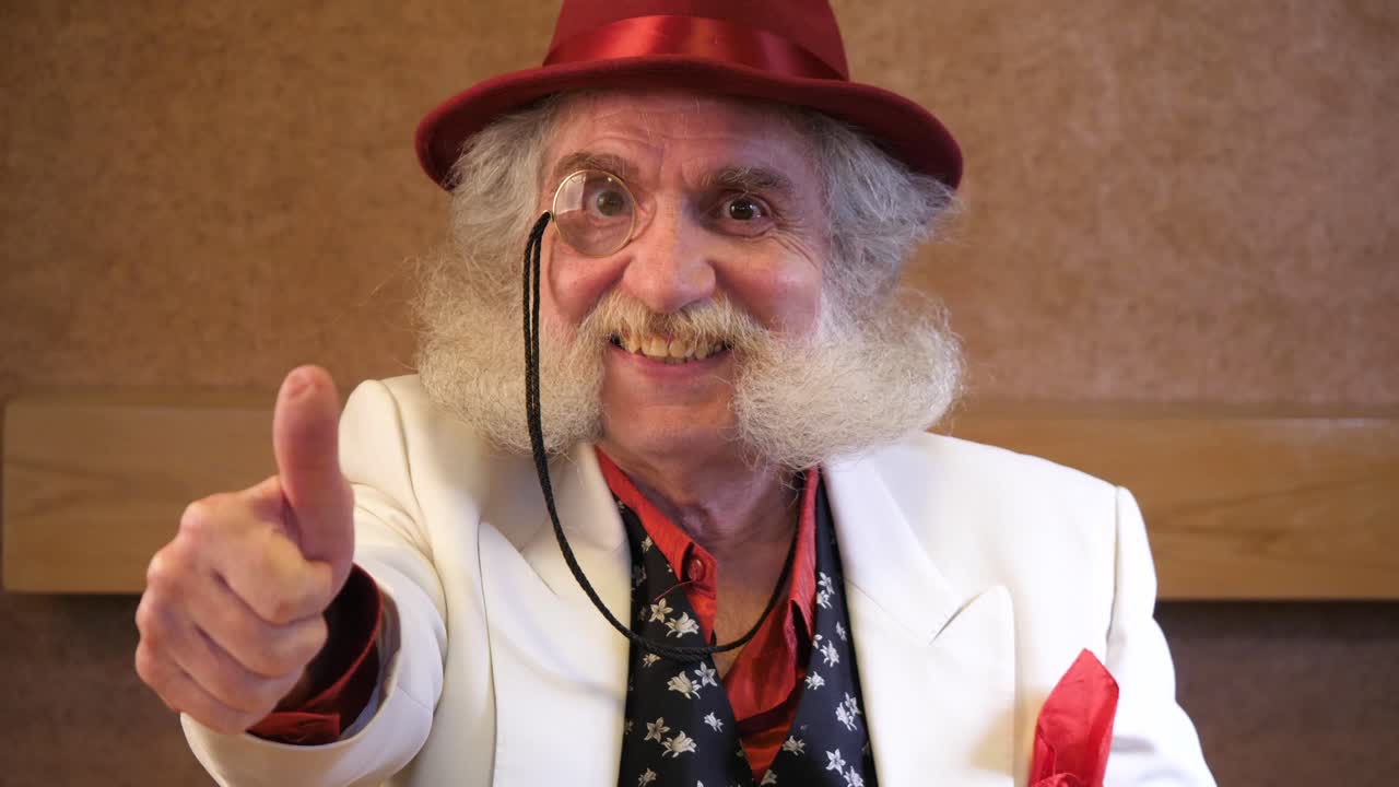 un hombre mayor con barba elegante se pone un monóculo y le da el visto bueno a la cámara